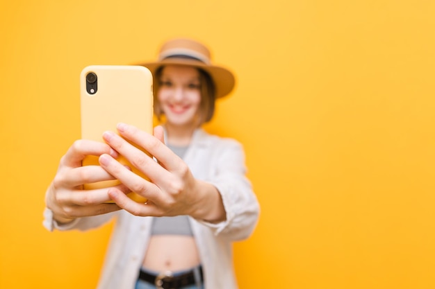 Turista feliz em roupas leves e chapéu faz selfie em fundo amarelo