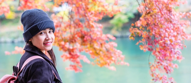 Turista feliz mirando hojas coloridas y el río Katsura en Arashiyama, joven viajero asiático visita Kioto y disfruta de viajar en Japón Temporada de otoño Concepto de vacaciones y turismo