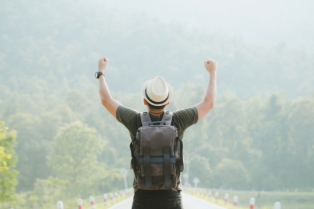 Turista feliz con una mochila levantando las manos en el aire en un saludo de victoria en el bosque