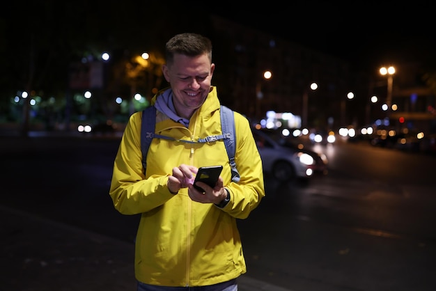 Turista feliz que usa la aplicación de viaje móvil en la calle de la ciudad, el hombre sostiene su teléfono inteligente y mira