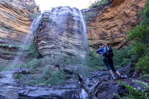 El turista femenino con el bolso de la mochila toma la foto en la cascada de Wentworth Falls