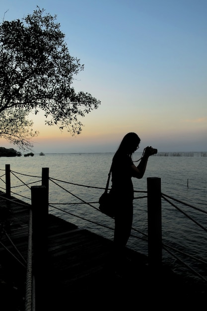 Un turista femenino tomar una foto del mar hermoso en el momento del crepúsculo.