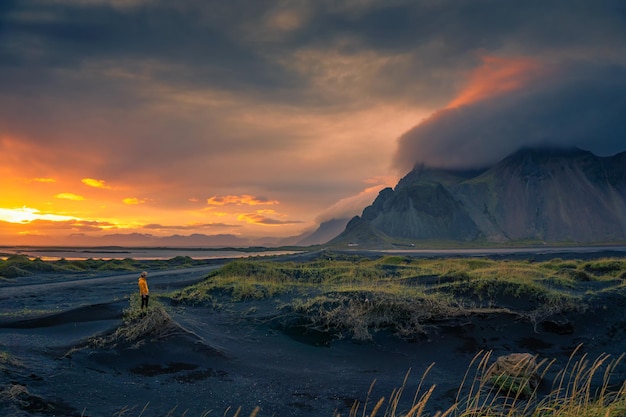 Turista fica em uma duna de areia na montanha Vestrahorn na Islândia ao pôr do sol