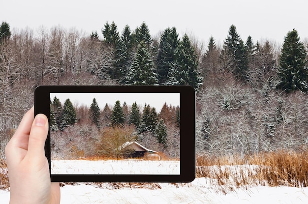 Turista fotografa casa de madeira na floresta nevada