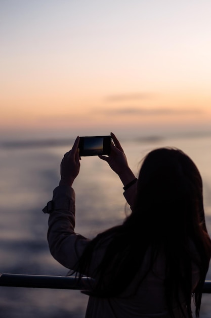 Turista fotografa um transatlântico ao pôr do sol no lago na Noruega Turista tira o pôr do sol no telefone