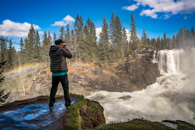 Turista fotógrafo de la naturaleza con tomas de cámara mientras está de pie La cascada Ristafallet en la parte occidental de Jamtland está catalogada como una de las cascadas más hermosas de Suecia.