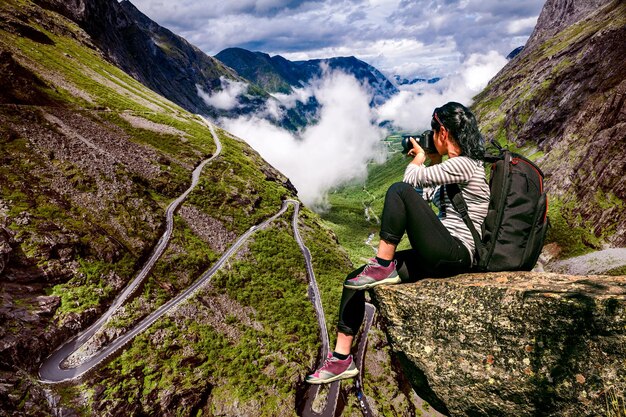 Turista fotógrafo de la naturaleza con tomas de cámara mientras está de pie en la cima de la montaña. Troll's Path Trollstigen o Trollstigveien sinuoso camino de montaña en Noruega.