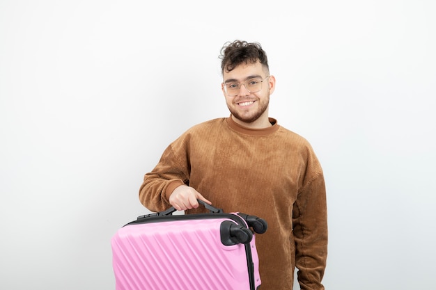 un turista guapo sosteniendo una maleta de viaje rosa.