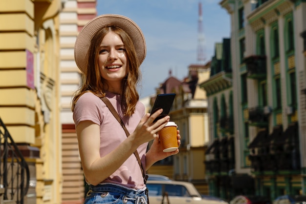 Turista hermosa joven con café para llevar en el centro de la ciudad hablando por teléfono.