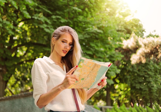 Turista hermosa mujer en ropa de estilo casual con mapa de la ciudad mientras camina por una ciudad desconocida