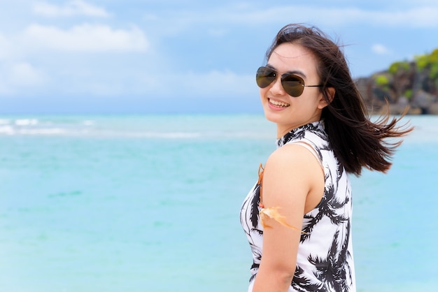 Turista hermosa mujer vistiendo sunglasse mirando a la cámara y sonriendo con feliz en la playa y el mar en el fondo del cielo de verano en la isla de Koh Tarutao, Satun, Tailandia