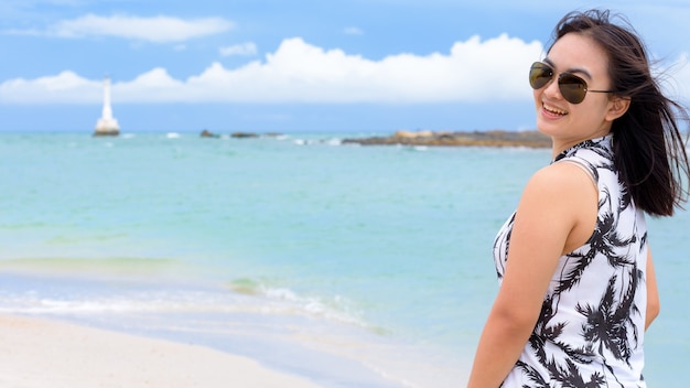 Turista hermosa mujer vistiendo sunglasse mirando a la cámara y sonriendo con feliz en la playa y el mar en el fondo del cielo de verano en la isla de Tarutao, Satun, Tailandia, 16: 9