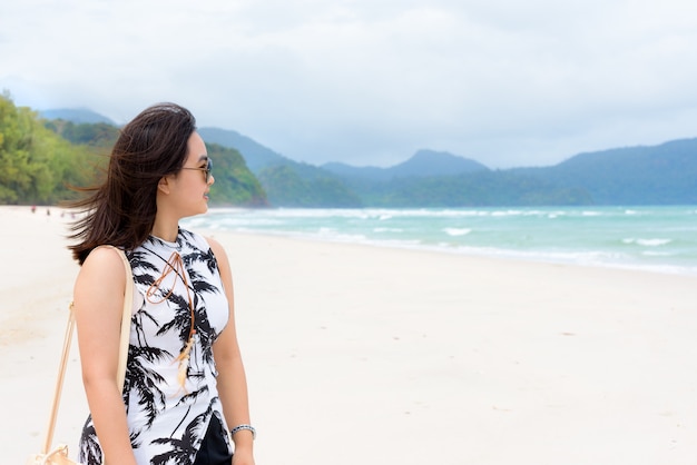 Turista hermosa mujer vistiendo sunglasse sonriendo mirando el paisaje natural de la playa y el mar en el cielo de verano en el Parque Nacional de la isla de Tarutao, Satun, Tailandia