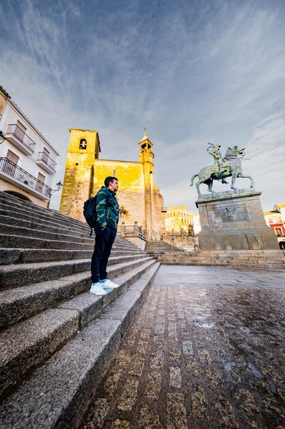 Turista hispânico explora a praça de Trujillo encantado com a igreja do pôr-do-sol e as poças de chuva