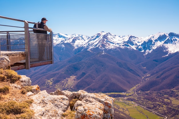 Un turista de hombre se encuentra en un mirador sobre un valle contra montañas cubiertas de nieve. Parque Nacional de los Picos de Europa, Cantabria, ESPAÑA