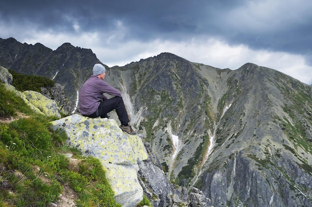 Turista hombre está sentado sobre una roca en las montañas