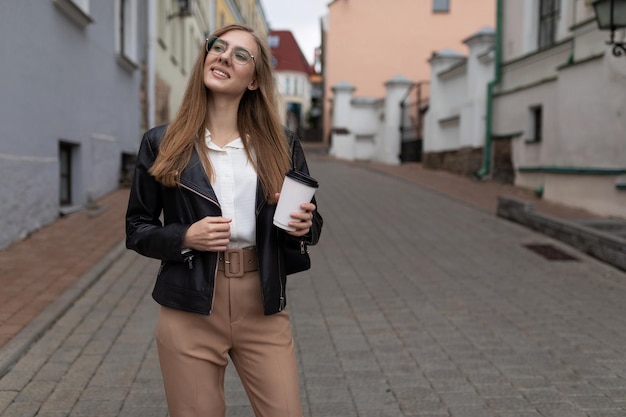 Turista jovem caminha pela cidade com uma xícara de café nas mãos e um telefone