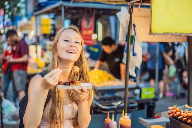 Turista jovem comendo comida de rua coreana típica em uma rua ambulante de seul fast food picante