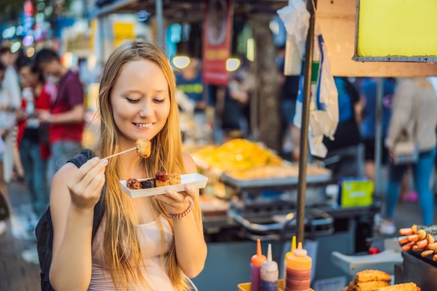 Turista jovem comendo comida de rua coreana típica em uma rua ambulante de seul fast food picante