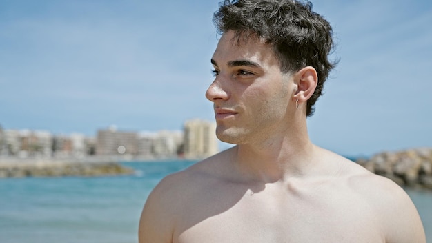 Turista jovem hispânico sorrindo confiante em pé na praia