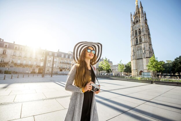 Turista joven caminando con photocamera en la plaza Pey-Berland con el campanario en el fondo durante la mañana en la ciudad de Burdeos