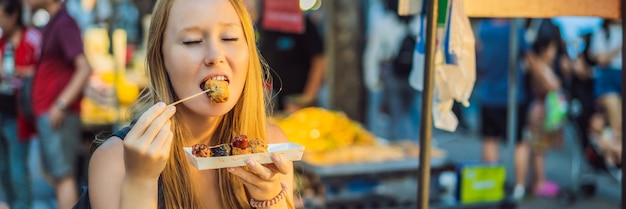 Turista joven comiendo comida callejera típica coreana en una calle peatonal de comida rápida picante de seúl