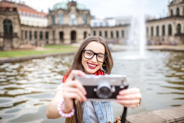 Turista joven y feliz sentado con cámara de fotos en la fuente en el casco antiguo de Dresde, Alemania