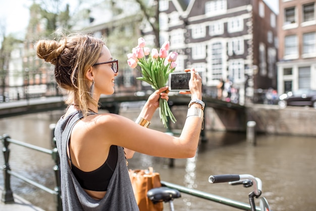 Turista joven fotografiando hermosos edificios en el canal del agua en la ciudad de Amsterdam