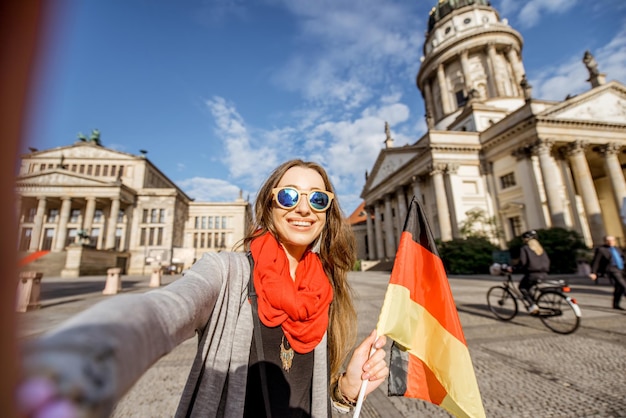 Turista joven haciendo foto selfie con bandera alemana en la iglesia francesa y el fondo de la ópera en Berlín.