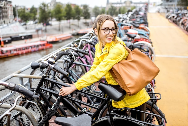 Turista joven en impermeable amarillo aparcar una bicicleta en el aparcamiento multinivel en Amsterdam