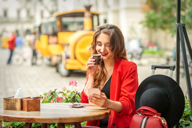 Turista joven mujer caucásica en chaqueta roja con taza de café en la mesa en el café al aire libre