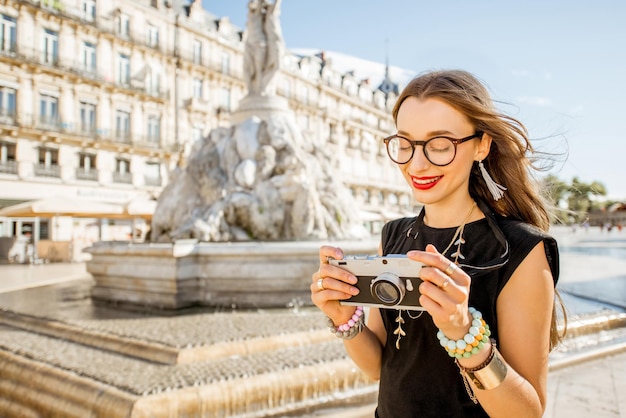 Turista joven de pie con cámara de fotos en la plaza de la comedia con la fuente principal en el fondo en la ciudad de Montpellier, Francia