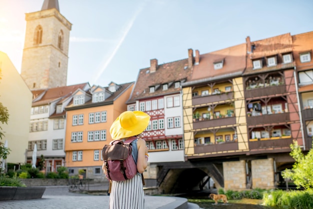 Turista joven con sombrero amarillo de pie en el famoso puente de los comerciantes de fondo en la ciudad de Erfurt, Alemania