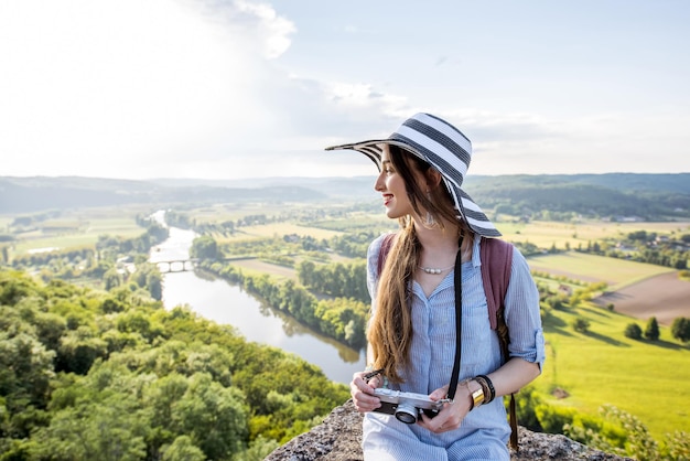 Turista joven con sombrero disfrutando de la vista del atardecer sobre el hermoso paisaje con el río Dordogne en Francia