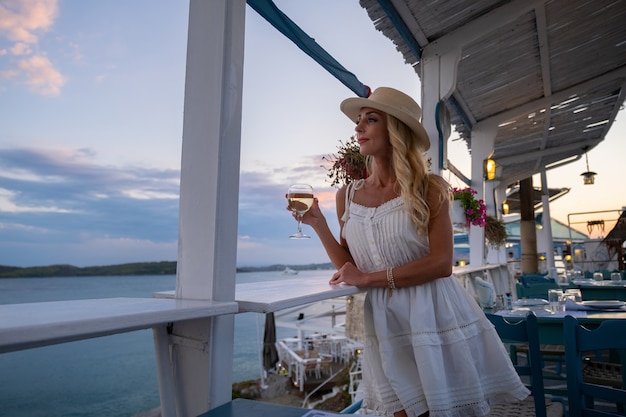 Turista joven en sombrero de paja sentado en el café del acantilado con vistas al mar en ermioni grecia