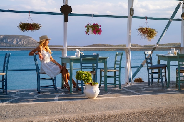 Turista joven en sombrero de paja sentado en el café en la marina de ermioni grecia