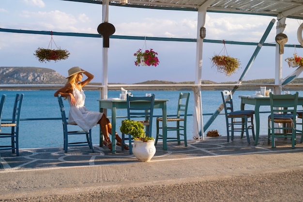 Turista joven en sombrero de paja sentado en el café en la marina de ermioni grecia