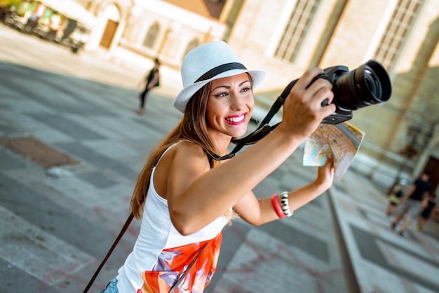 Turista linda jovem segurando o mapa e fotografando com câmera digital.