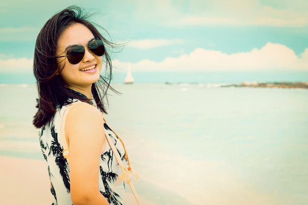 Turista linda mulher vestindo sunglasse sorrindo olhando para a câmera na praia perto do mar no parque nacional da ilha de tarutao, satun, tailândia, em verde azulado e cor de laranja estilo vintage