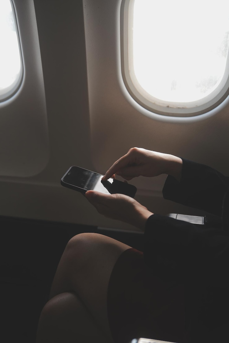 Foto turista loira verificando notificação de entrada no smartphone sentada no assento do avião com netbook mulher de negócios jovem compartilha mídia do telefone no computador portátil durante o voo de avião