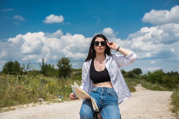 Turista con un mapa caminando por una carretera en un día soleado de verano