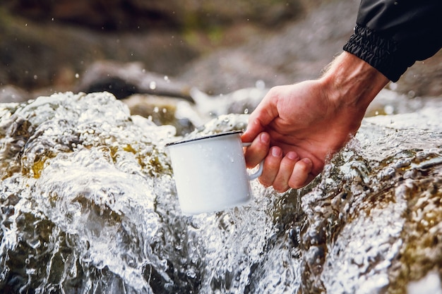 Turista masculina carregando uma caneca de metal no contexto dos rios turva.