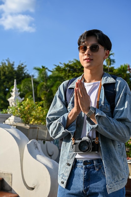Turista masculino asiático juntando as mãos em posição de oração no templo
