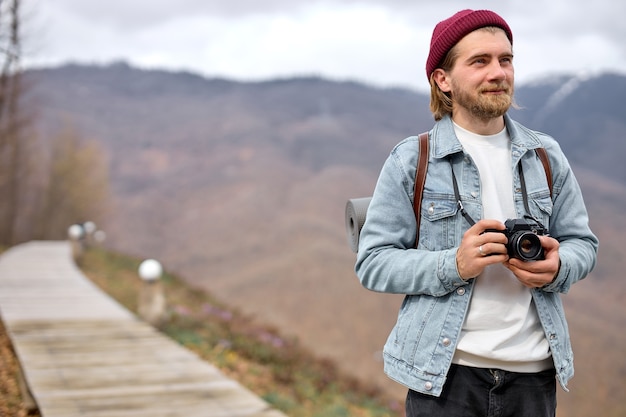 Turista masculino barbudo feliz com a câmera andando, tirando fotos, sorrindo, olhando para o lado