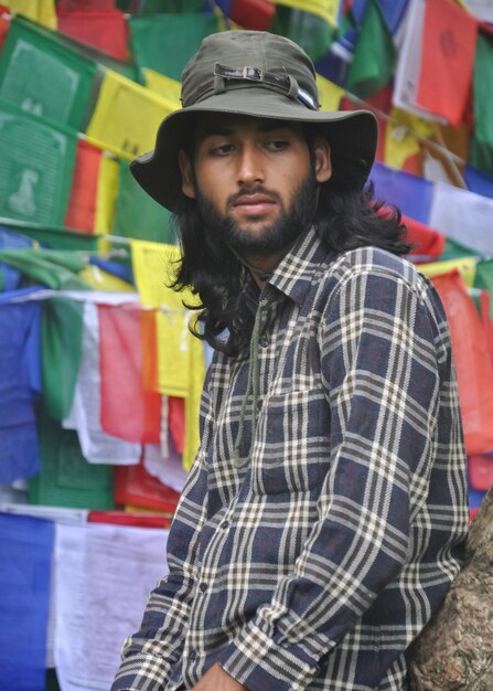 Foto un turista masculino de buen aspecto mirando hacia los lados mientras posa contra banderas de oración budistas