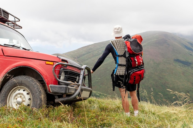 turista masculino com mochila e equipamento de caminhada com carro nas montanhas