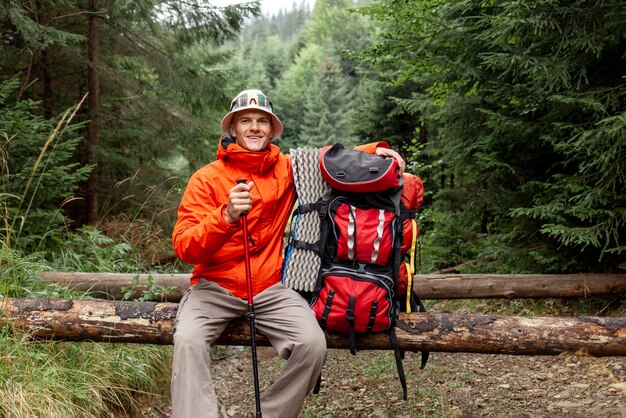 turista masculino com mochila e equipamento de caminhada senta-se descansando na floresta cara em jaqueta laranja