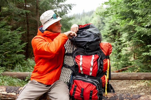 Foto turista masculino con mochila y equipo de senderismo se sienta descansando en el bosque tipo en chaqueta naranja