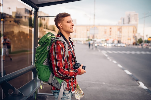 Turista masculino con mochila en la parada de autobús. Viajes de verano, caminatas de aventura con turismo, caminatas por la ciudad