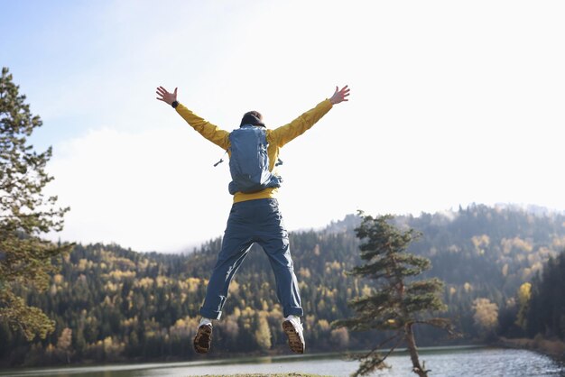 Turista masculino salta sobre la orilla del gran lago en el bosque salvaje